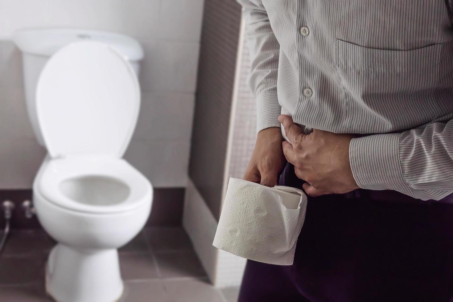 homem segurando tecido perto de um vaso sanitário - problema de saúde do estômago foto