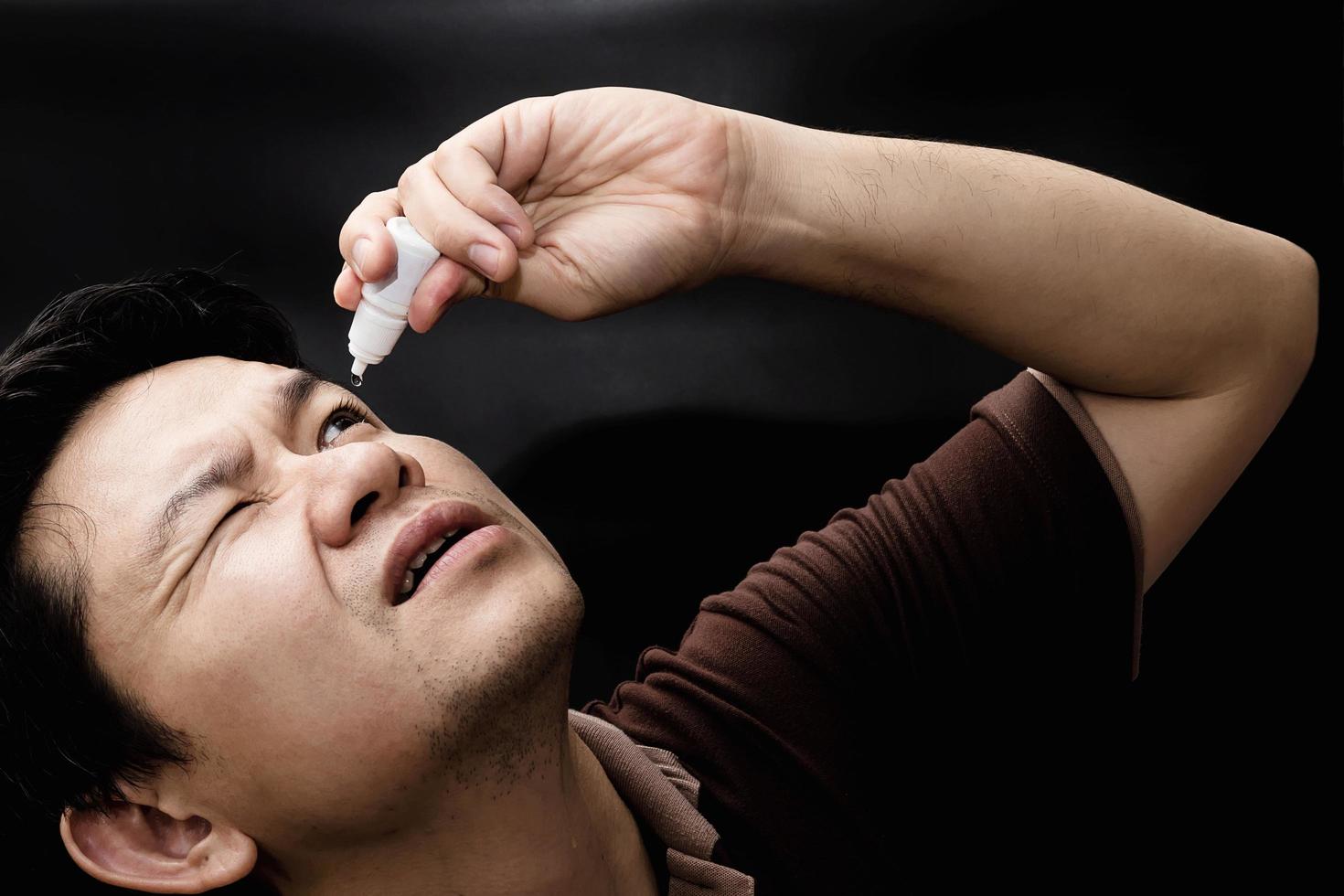homem soltando remédio de colírio curando sua dor nos olhos com fundo preto - remédio oftalmológico de cuidados de saúde com conceito de pessoas foto