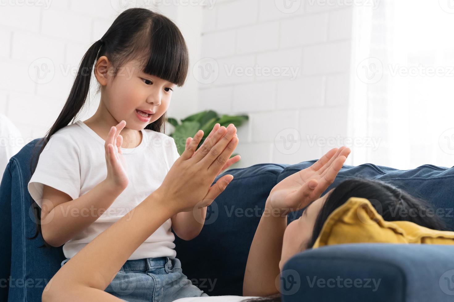 linda garota asiática gosta de brincar com a mãe no sofá azul. foto