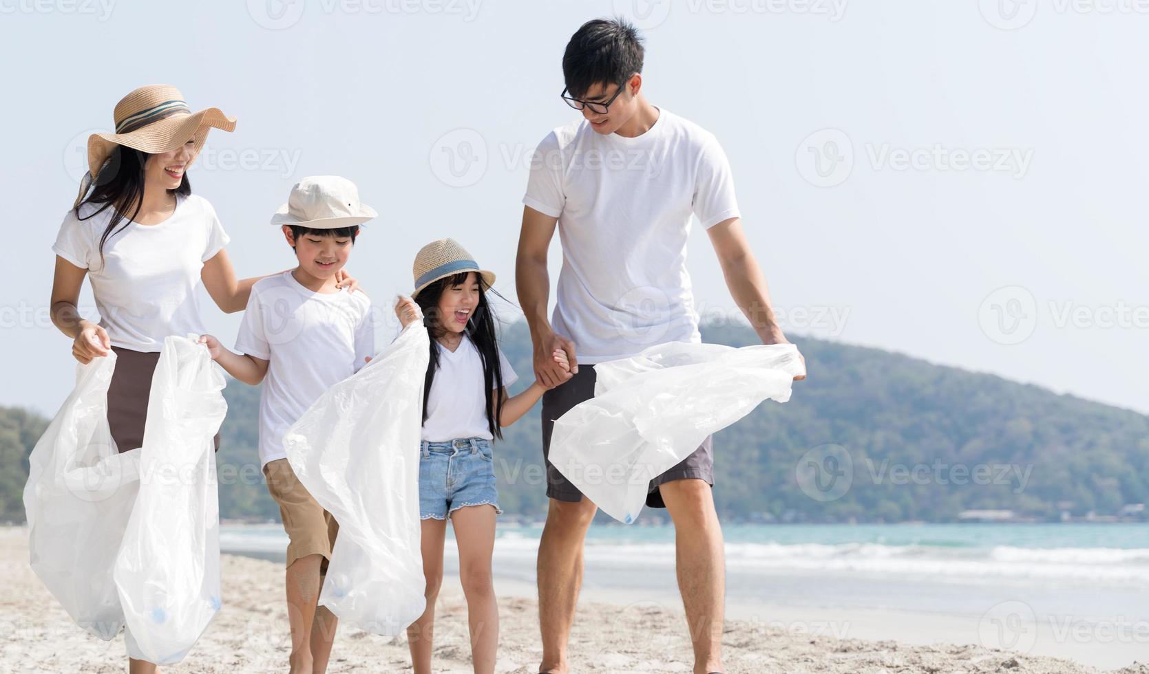 voluntário da família asiática pegando uma garrafa de plástico em uma praia com mar para proteger o meio ambiente foto