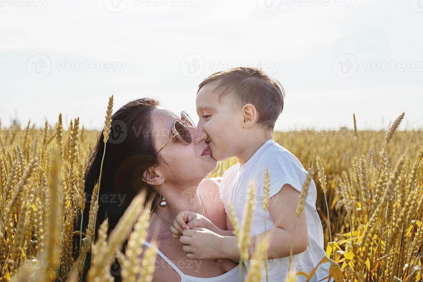 família feliz de mãe e criança caminhando no campo de trigo beijando foto