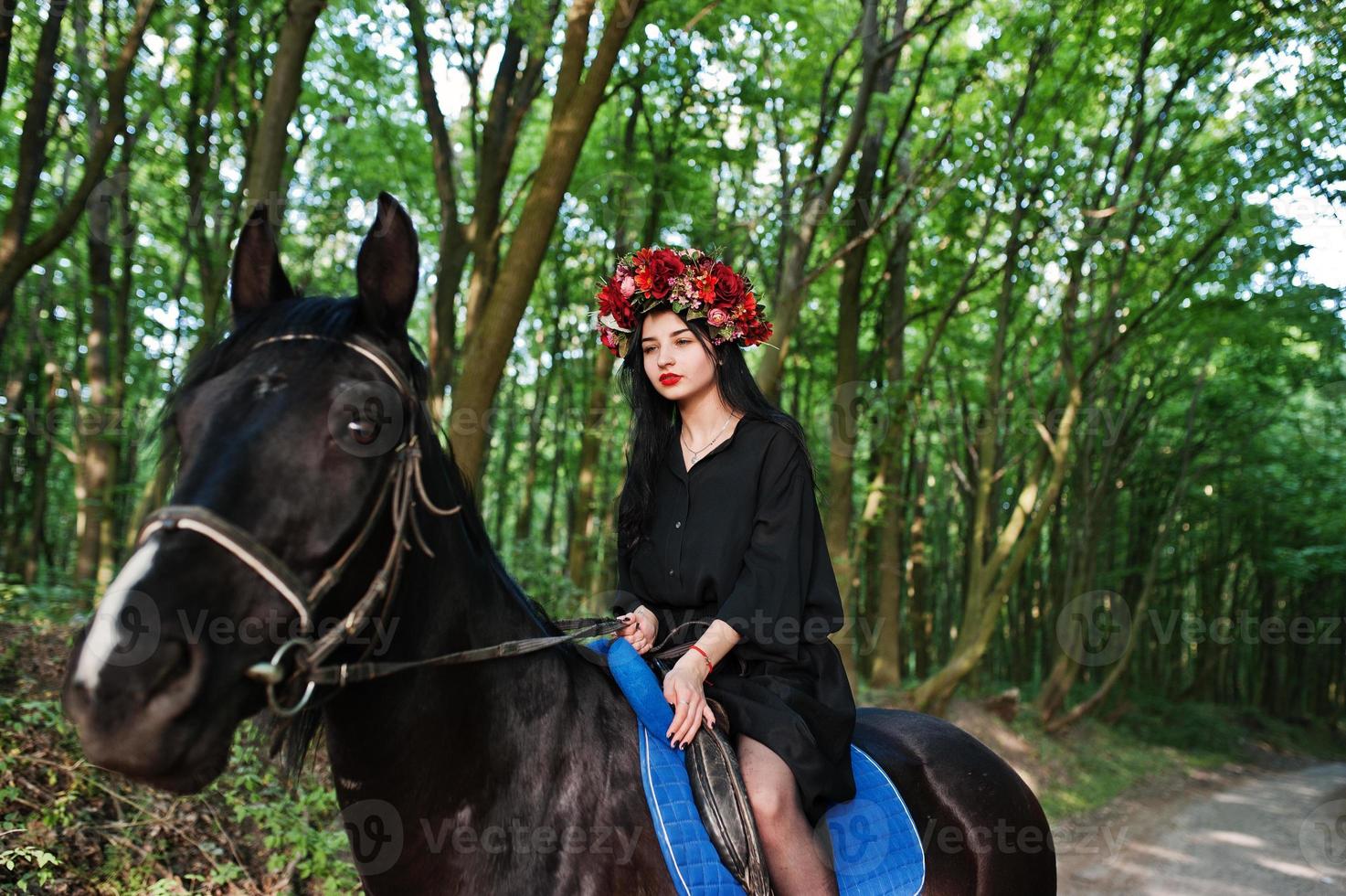 garota mística em grinalda veste de preto a cavalo em madeira. foto