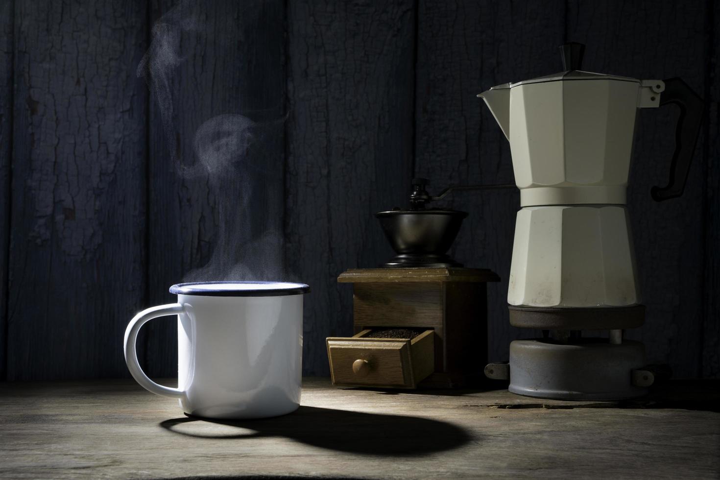 xícara de café esmaltada com fumaça. conjunto de café com bule de moka e moedor no antigo piso de madeira. foco suave. foto