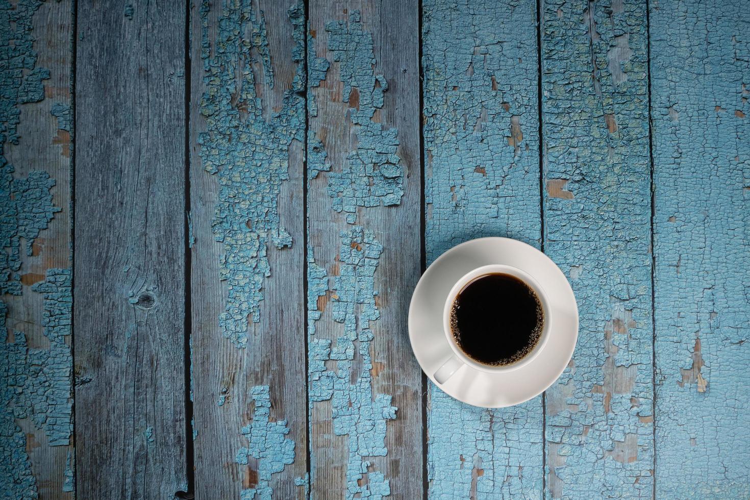 café preto em xícara de cerâmica branca no velho piso de madeira azul foto
