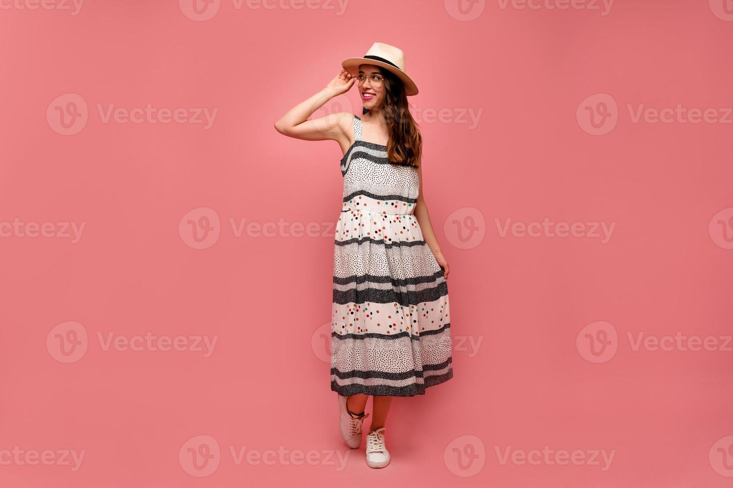 retrato de corpo inteiro de encantadora senhora usando chapéu de verão e vestido longo posando durante a sessão de fotos sobre fundo rosa. moda retrato mulher elegante