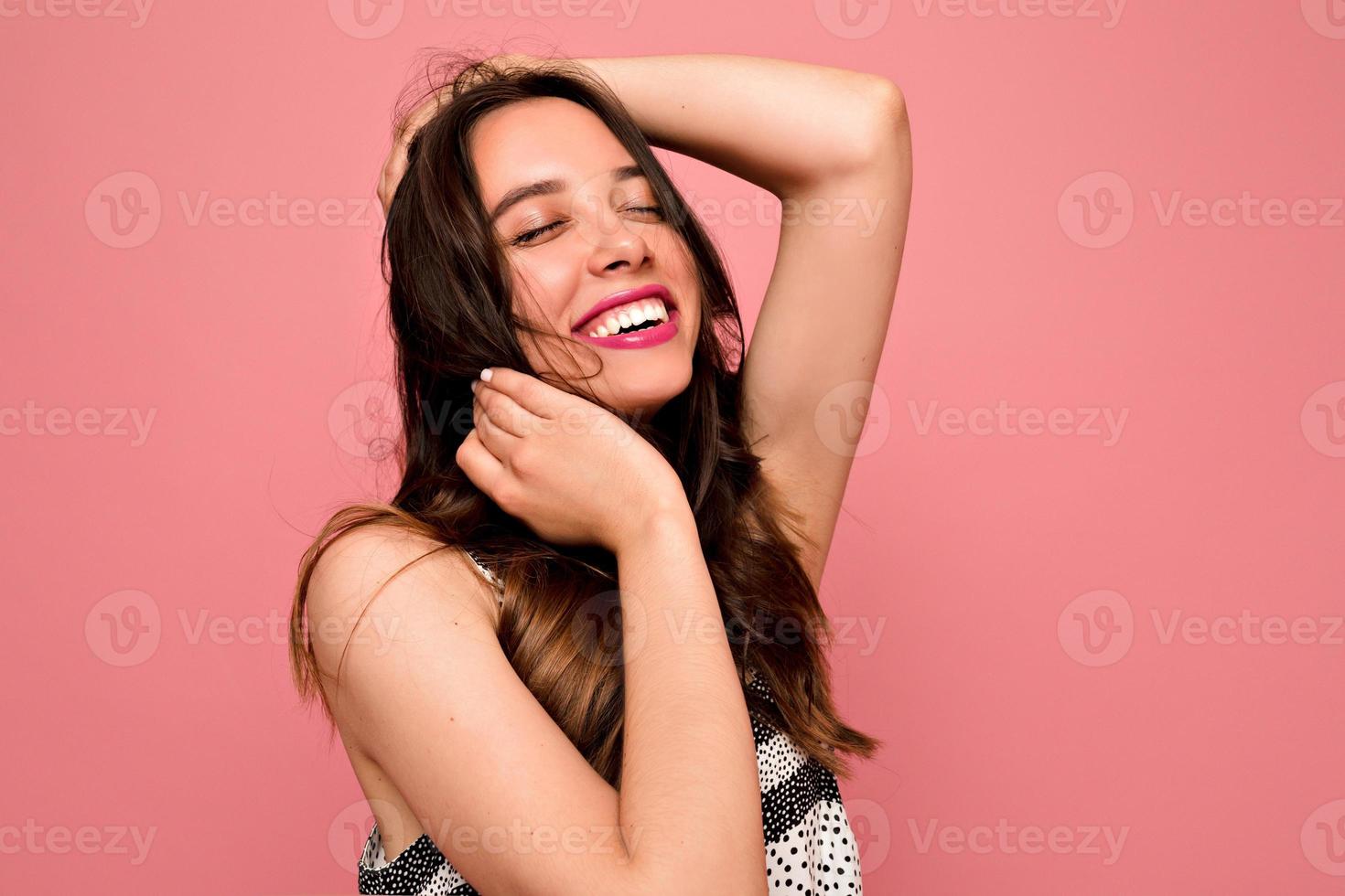 womna feliz animada com penteado ondulado e lábios cor de rosa posando com os olhos fechados e sorriso feliz vestido de verão vestido em fundo rosa, verdadeiras emoções felizes, clima de verão foto