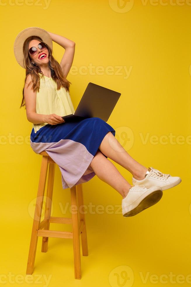 foto de corpo inteiro de garota relaxada usando vestido de verão brilhante trabalhando com laptop sentado na cadeira sobre fundo isolado