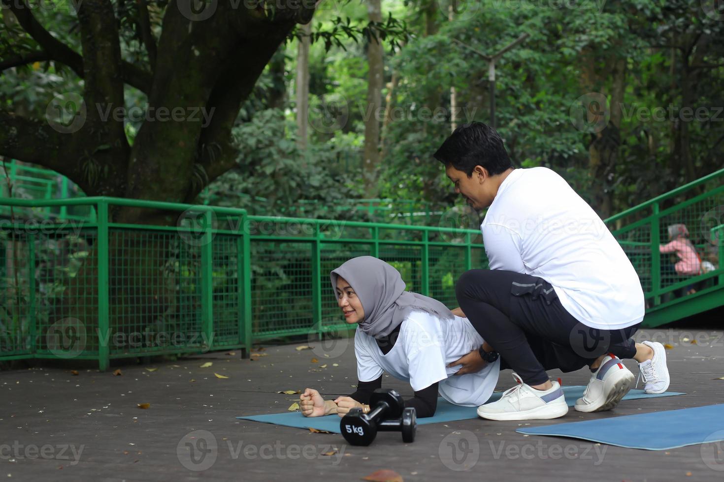 jovem asiático ajudando sua esposa fazendo prancha no tapete de ioga no parque. conceito de casal de estilo de vida saudável. foto