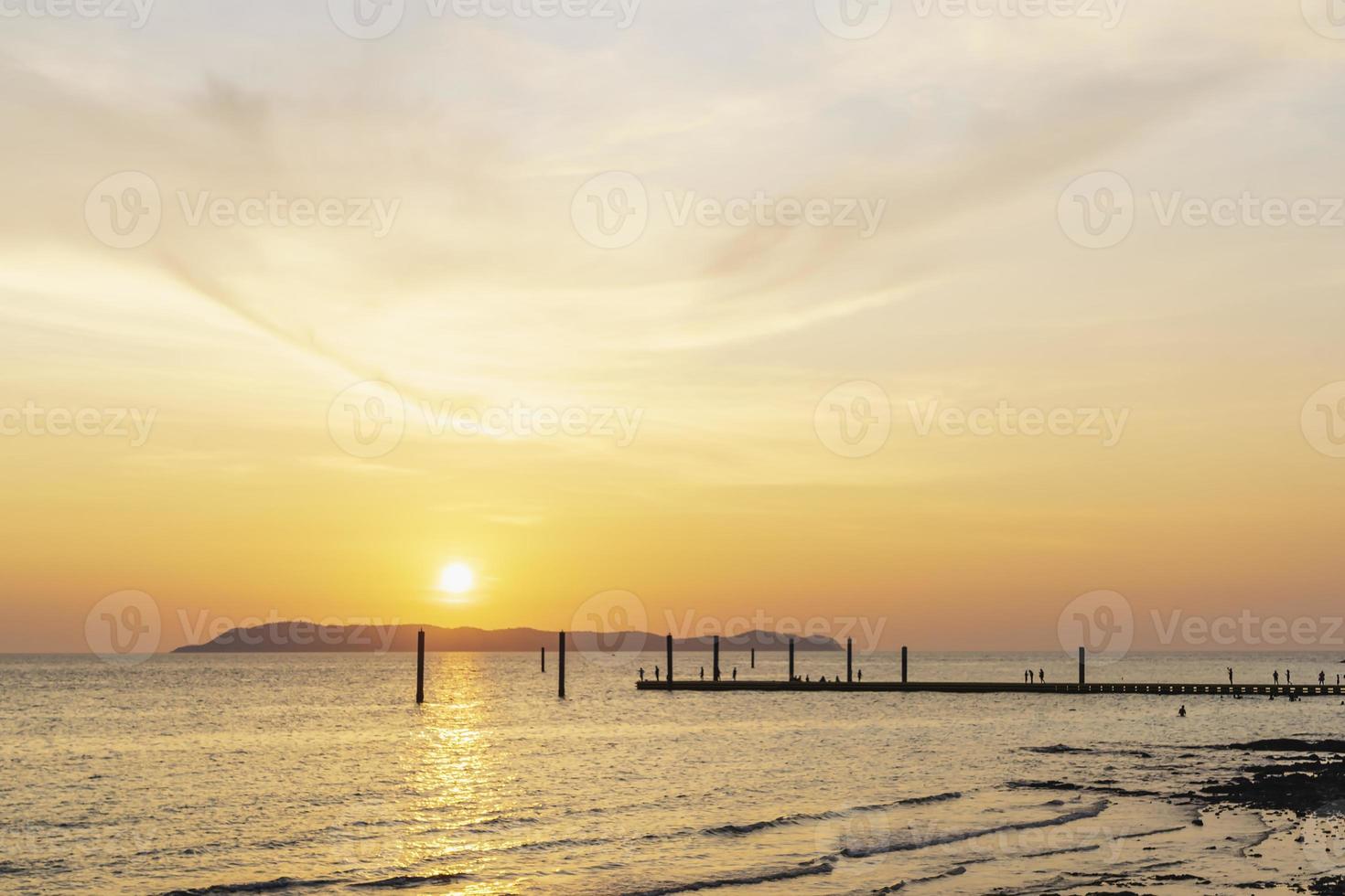 paisagem do pôr do sol colorido brilhando sobre as águas laranja brilhantes do oceano. silhueta de turistas caminhando, relaxando e tirando fotos ao pôr do sol na praia do pôr do sol tropical na praia de koh larn.