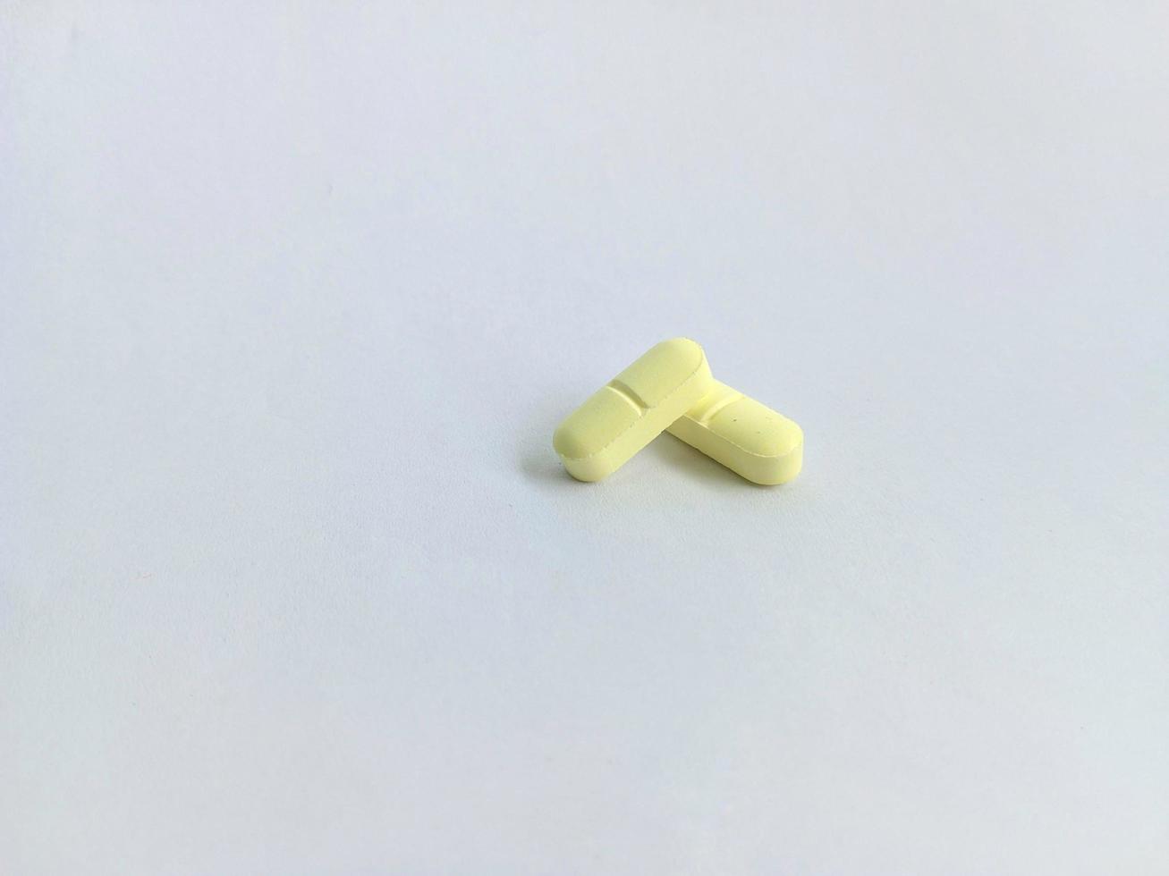 duas pequenas pílulas amarelas ou pílulas isoladas em um fundo branco ou em papel branco foto