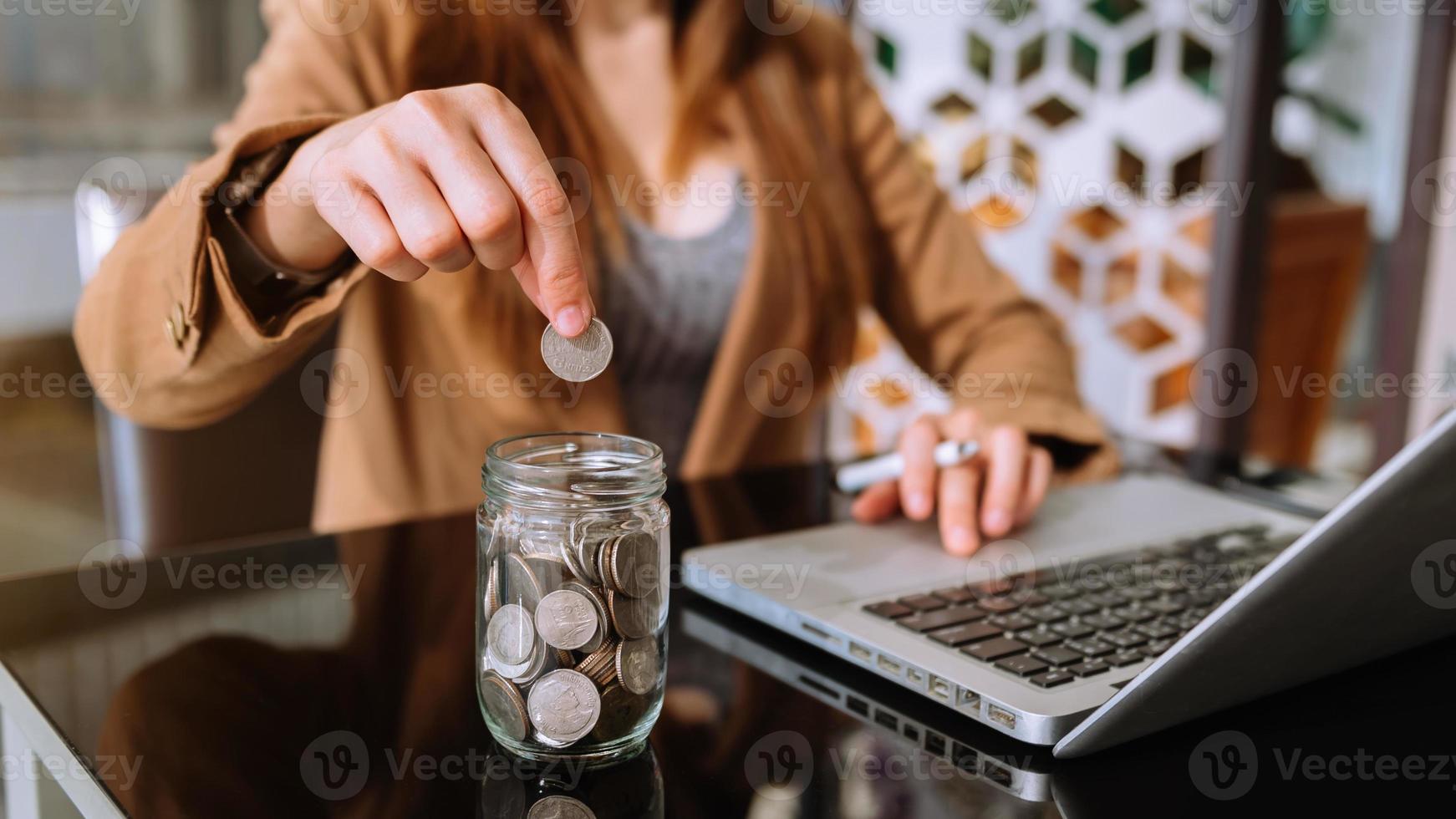 empresária segurando moedas colocando em vidro usando smartphone e calculadora para calcular o conceito de economia de dinheiro para finanças foto