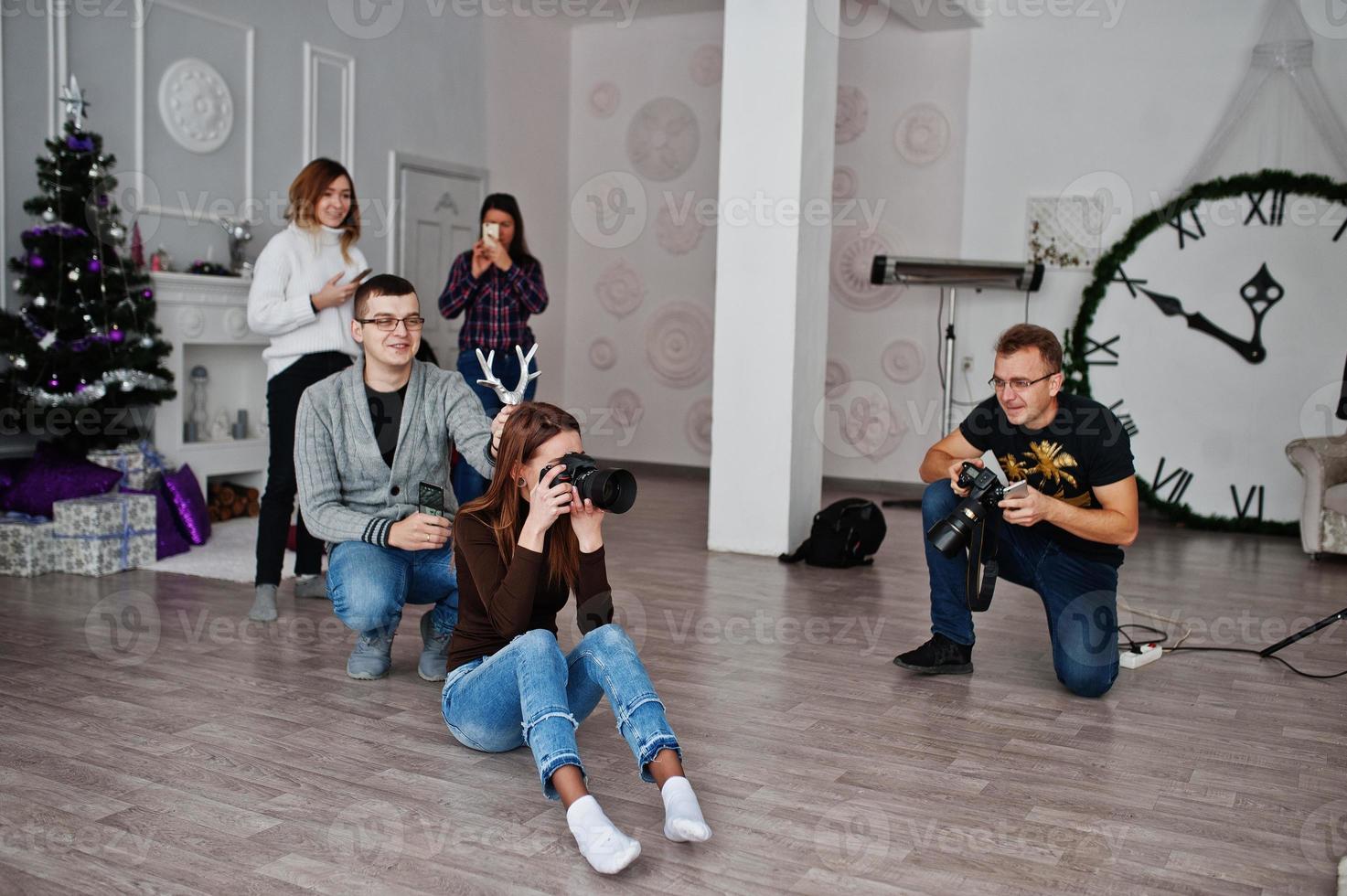 a equipe de dois fotógrafos fotografando em estúdio atrás de outros três trabalhadores. fotógrafo profissional no trabalho. um deles brincando e segura chifres na cabeça. foto