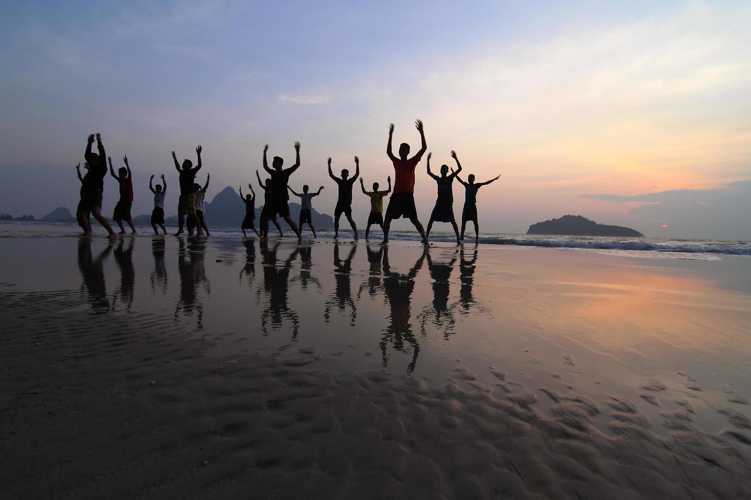 grupo de silhuetas de jovens felizes pulando na praia no belo pôr do sol de verão foto