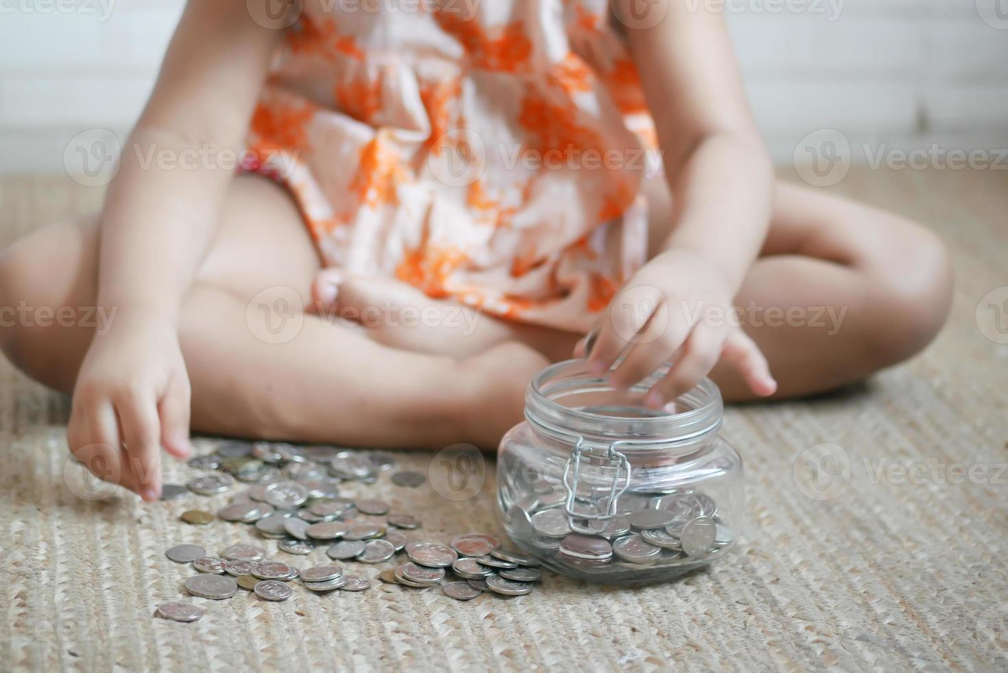 menina criança pilha moedas para economizar. sentado no chão foto