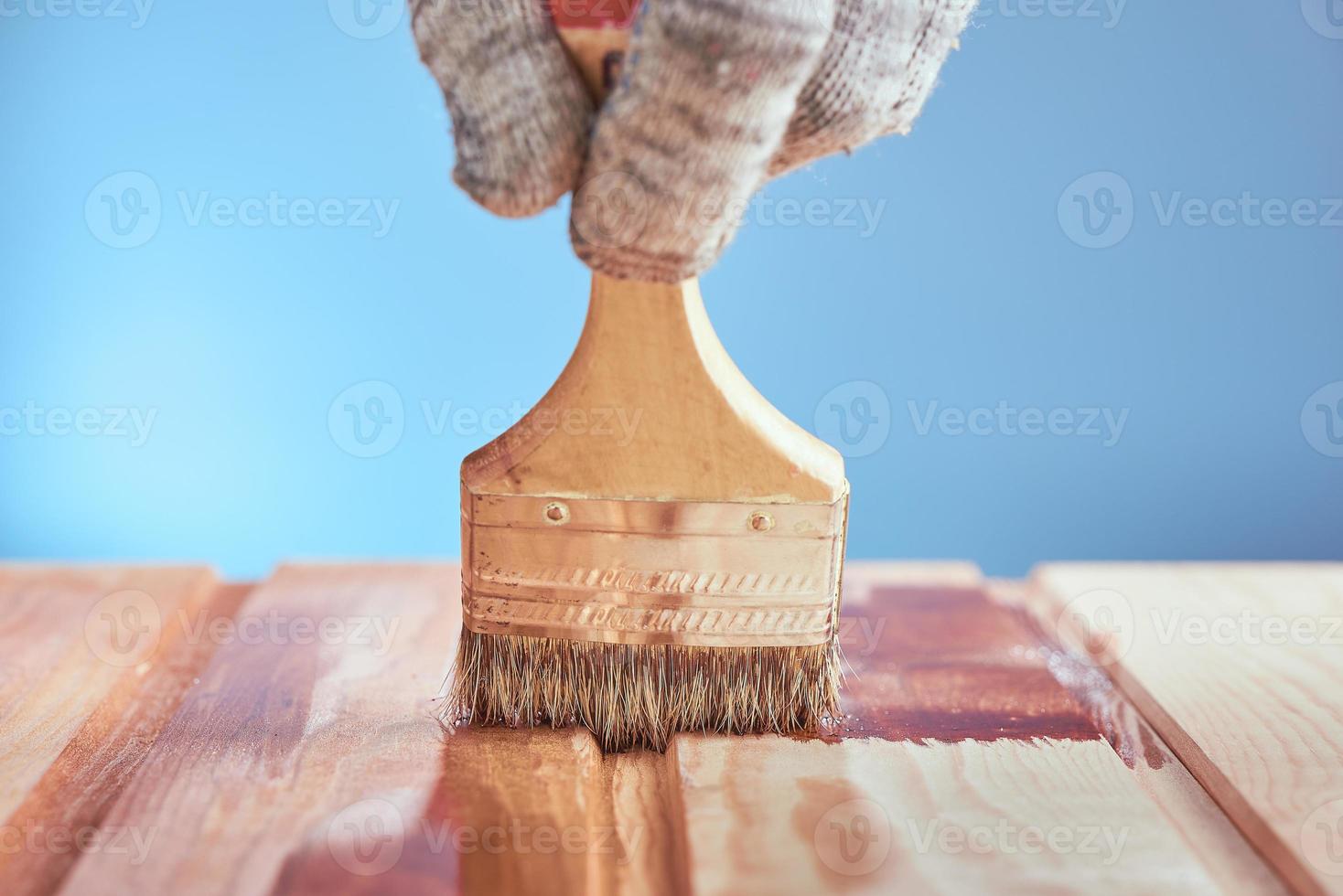 pintando piso de madeira com verniz protetor sobre fundo azul. foto