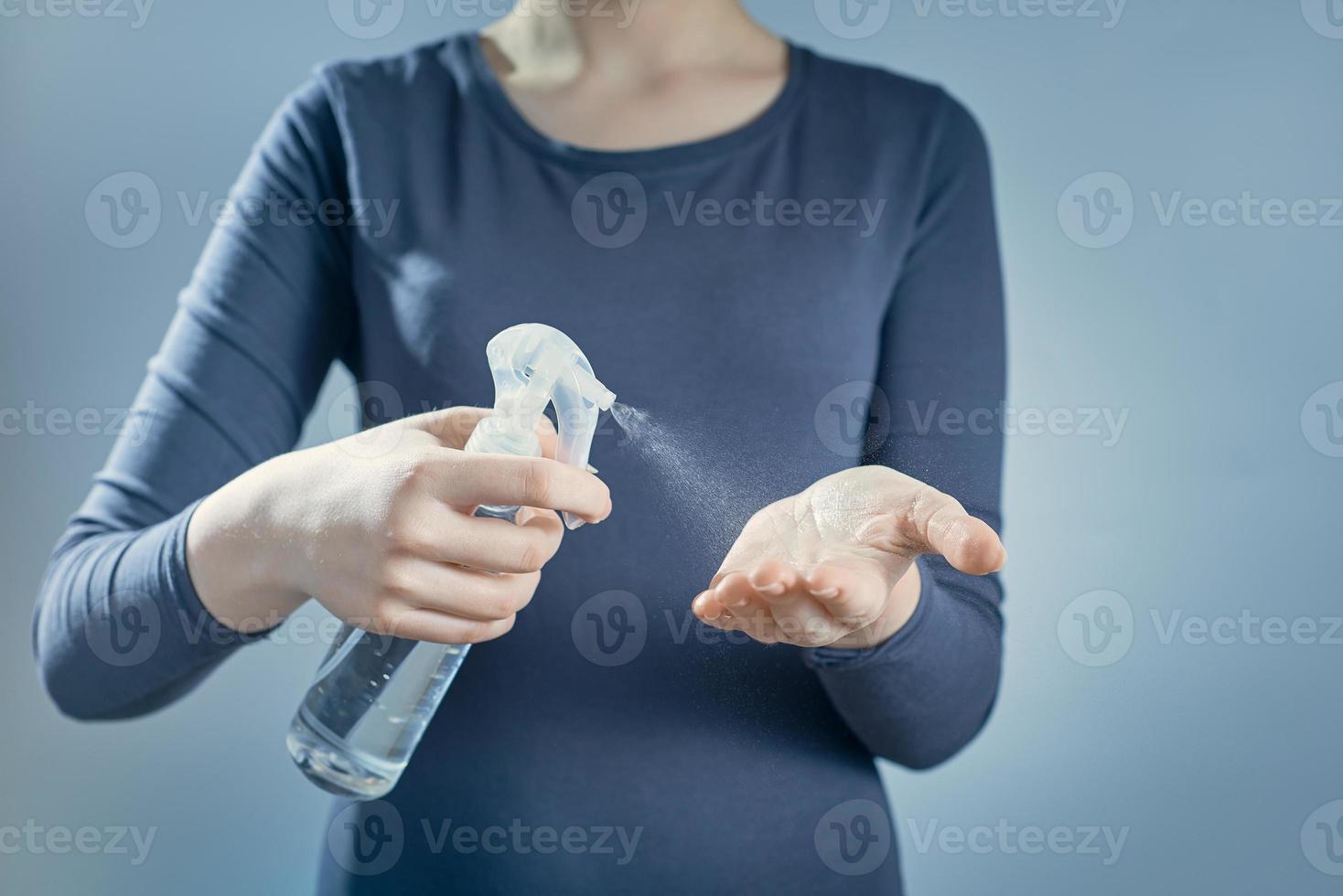 uma garota trata as mãos com desinfetante em fundo cinza. spray desinfetante no fundo de uma garota. foto