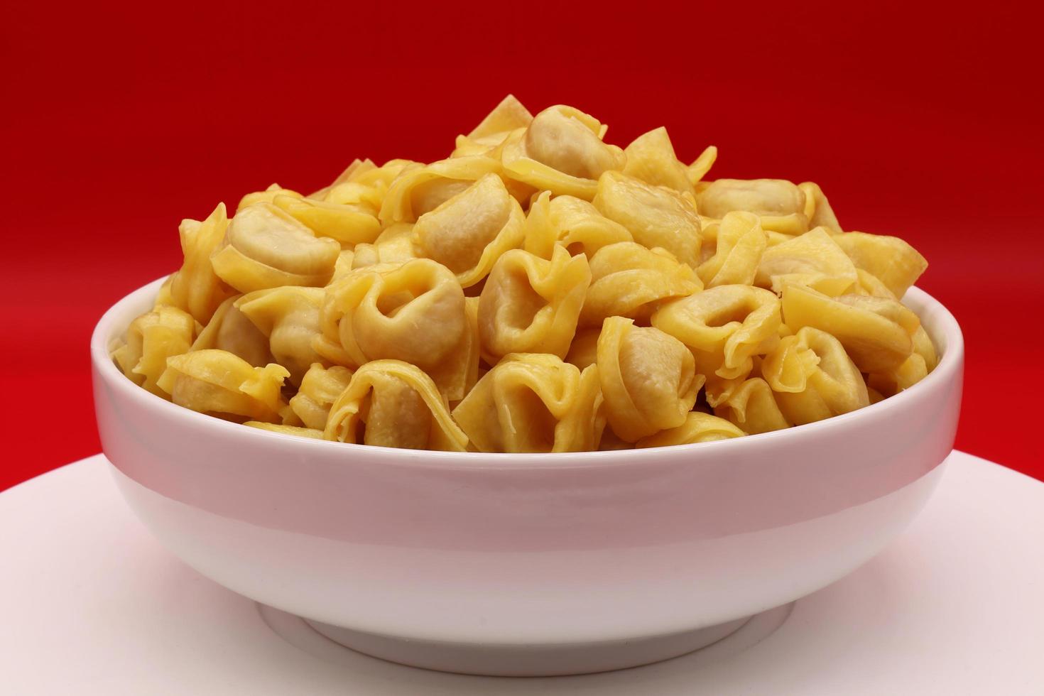 macarrão tortellini cru em uma tigela isolada em fundo vermelho. massa italiana tradicional foto