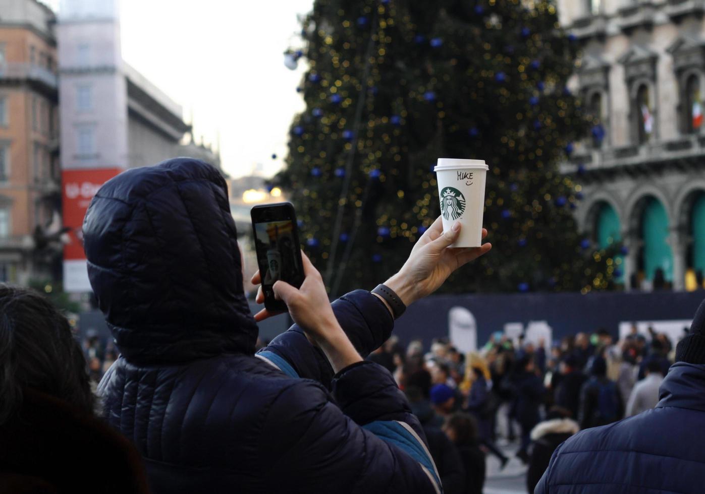 milão, itália - 14 de dezembro de 2019 - um jovem segura um copo de papel starbucks e tira uma foto dele com seu celular.