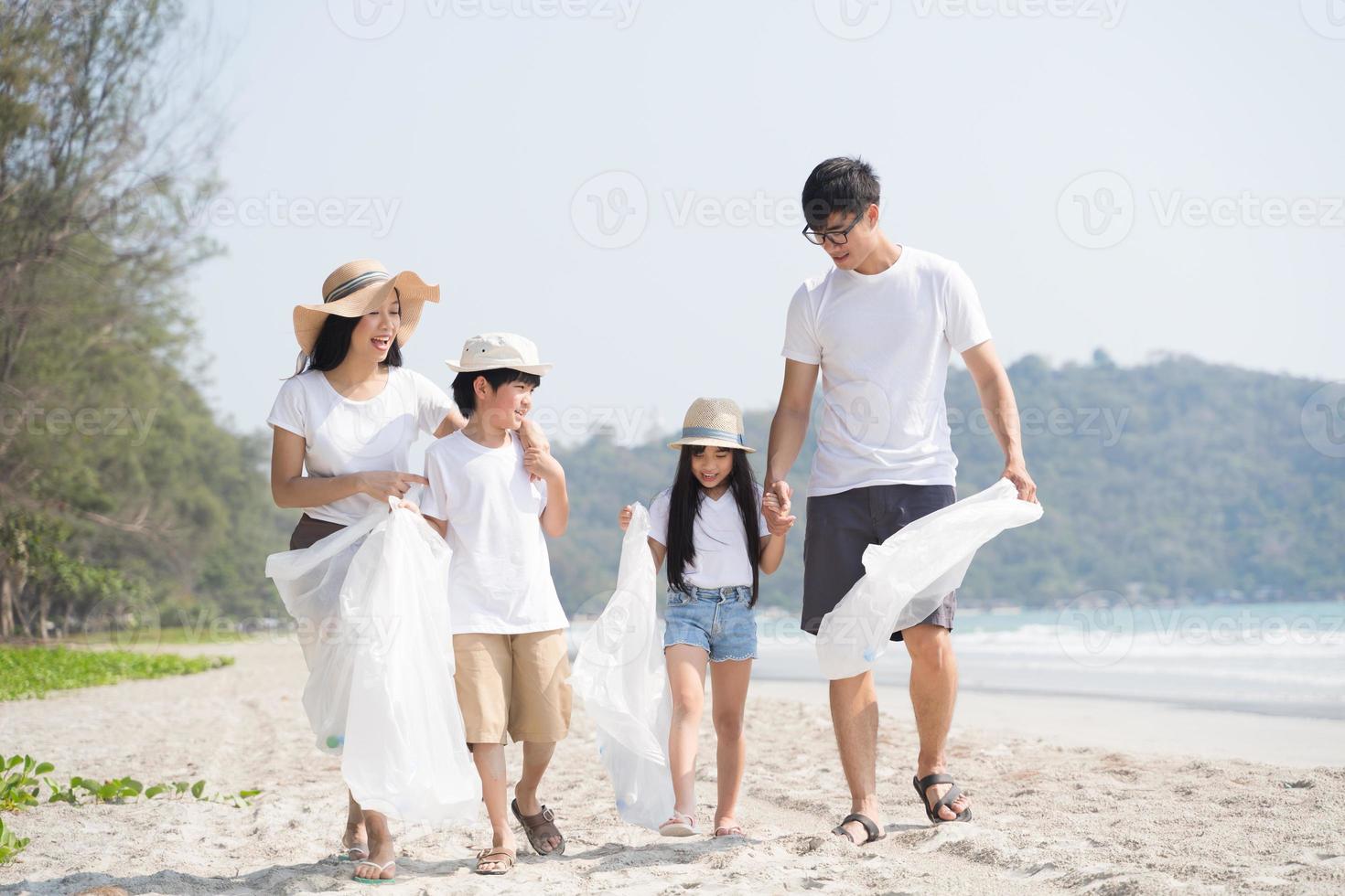 voluntário da família asiática pegando uma garrafa de plástico em uma praia com mar para proteger o meio ambiente foto