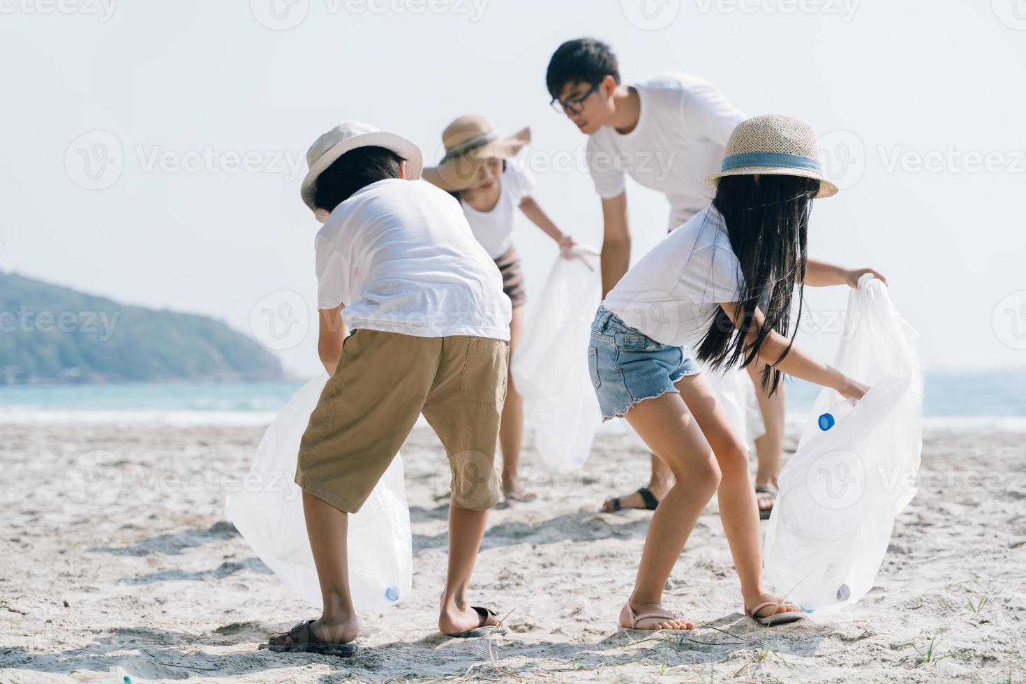 voluntário da família asiática pegando uma garrafa de plástico em uma praia com mar para proteger o meio ambiente foto