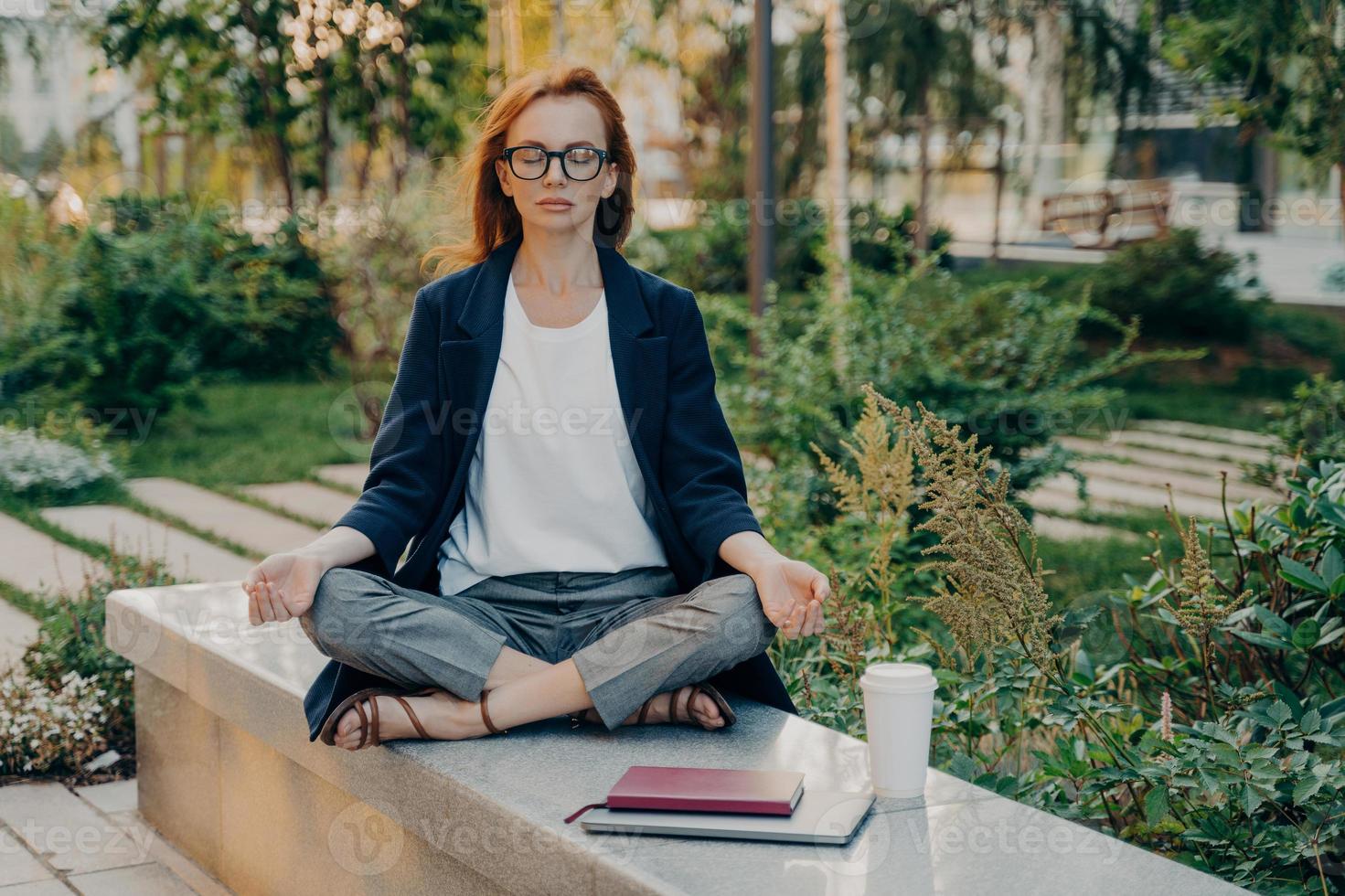 mulher ruiva realxed faz ioga lá fora no parque senta-se em pose de lótus medita ao ar livre foto