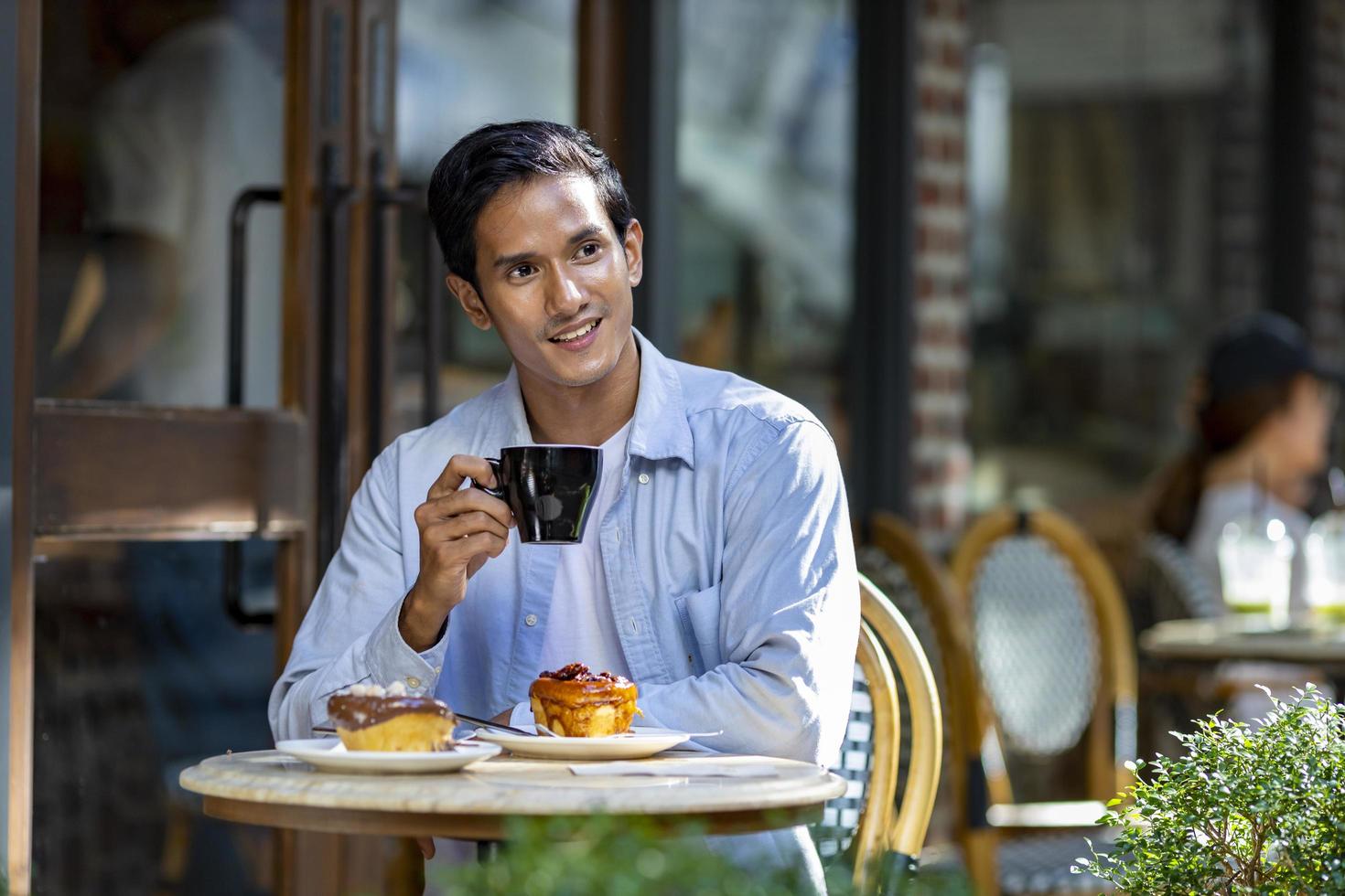 homem asiático tomando um café expresso quente enquanto está sentado do lado de fora do café bistrô de estilo europeu curtindo a vida lenta com vibração matinal na praça da cidade com pastelaria doce foto