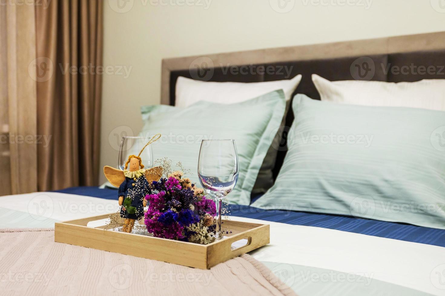 cama de casal com almofadas no interior do quarto íntimo em apartamento em apartamentos de estilo leve com decoração de natureza morta de dois copos de vinho vazios, brinquedo de anjo de pano caseiro e buquê de flores secas. foto