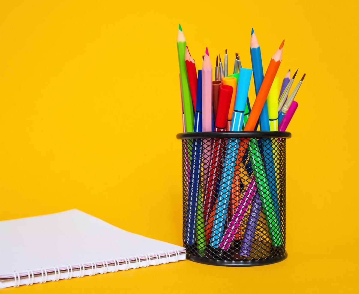 lápis de cor em uma caixa de lápis em um fundo amarelo com uma folha de papel branca foto