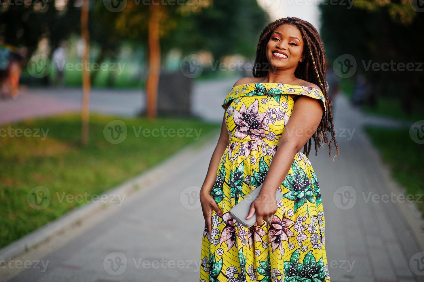 linda garota afro-americana de pequena altura com dreadlocks, use vestido amarelo colorido, posou ao pôr do sol. foto