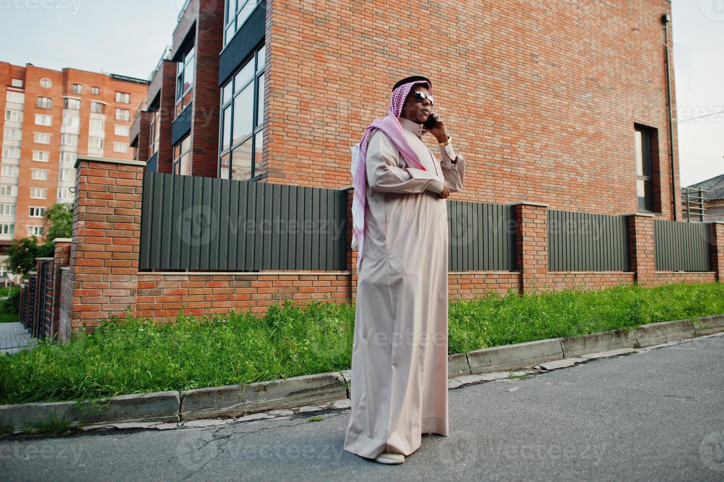 homem de negócios árabes do Oriente Médio posou na rua contra um edifício moderno com óculos de sol, falando no celular. foto