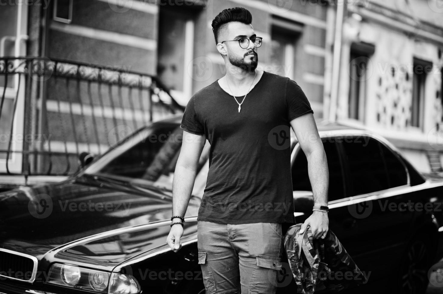 incrível lindo homem macho de barba árabe alta de óculos e camiseta preta andando contra o carro de negócios. foto