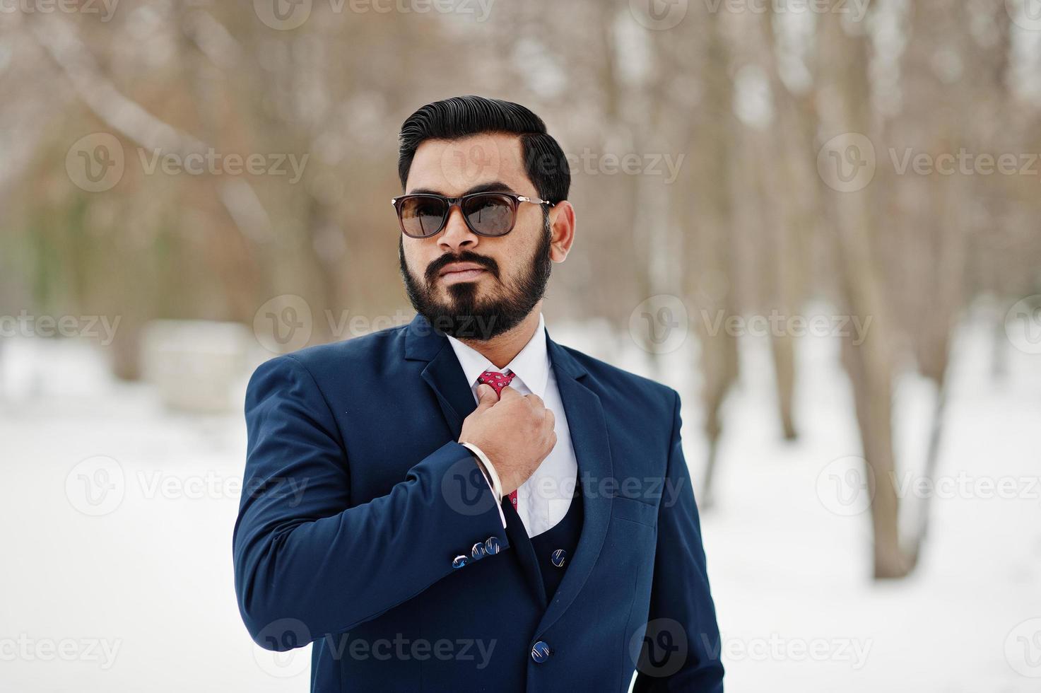 homem de negócios de barba indiana elegante de terno e óculos de sol posou em dia de inverno ao ar livre. foto