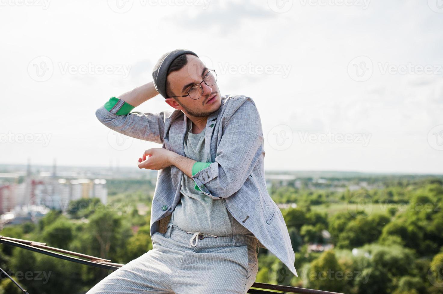 sonhador elegante macho de terno cinza, chapéu e óculos posou no telhado. foto