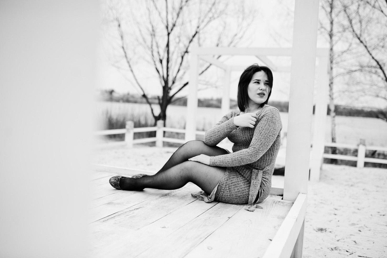 retrato de menina morena de vestido cinza, sentado na construção de madeira branca. foto