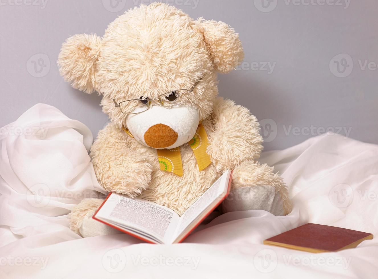 lindo ursinho de pelúcia bege para crianças brincando com óculos lê um livro foto