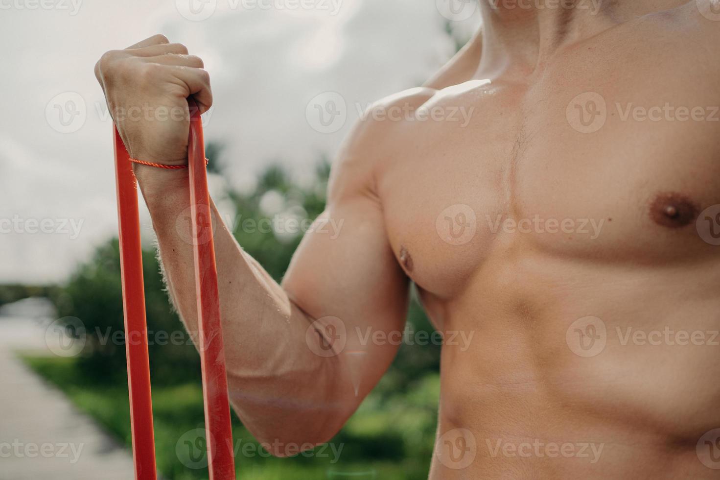 homem forte irreconhecível tem treino com banda de resistência, fica mais forte a cada dia, mostra corpo bem construído, poses ao ar livre. esporte, musculação e conceito de estilo de vida saudável. atleta sem rosto foto