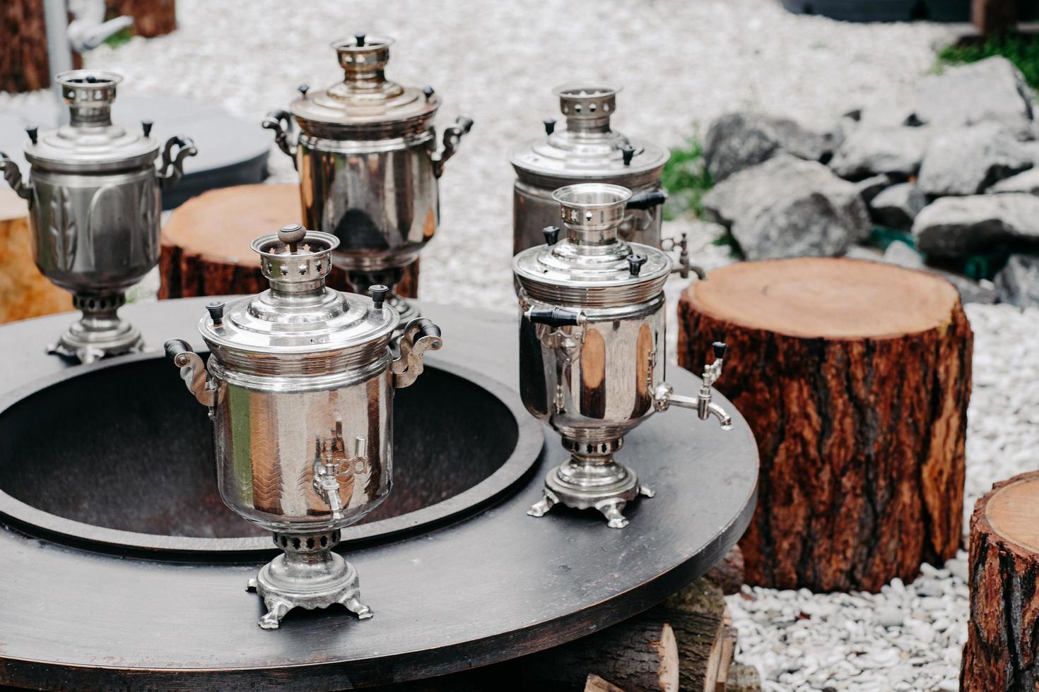 samovars de cobre antigos na superfície redonda com tocos de madeira ao ar livre. conceito de festa bebendo chá. tradição russa foto