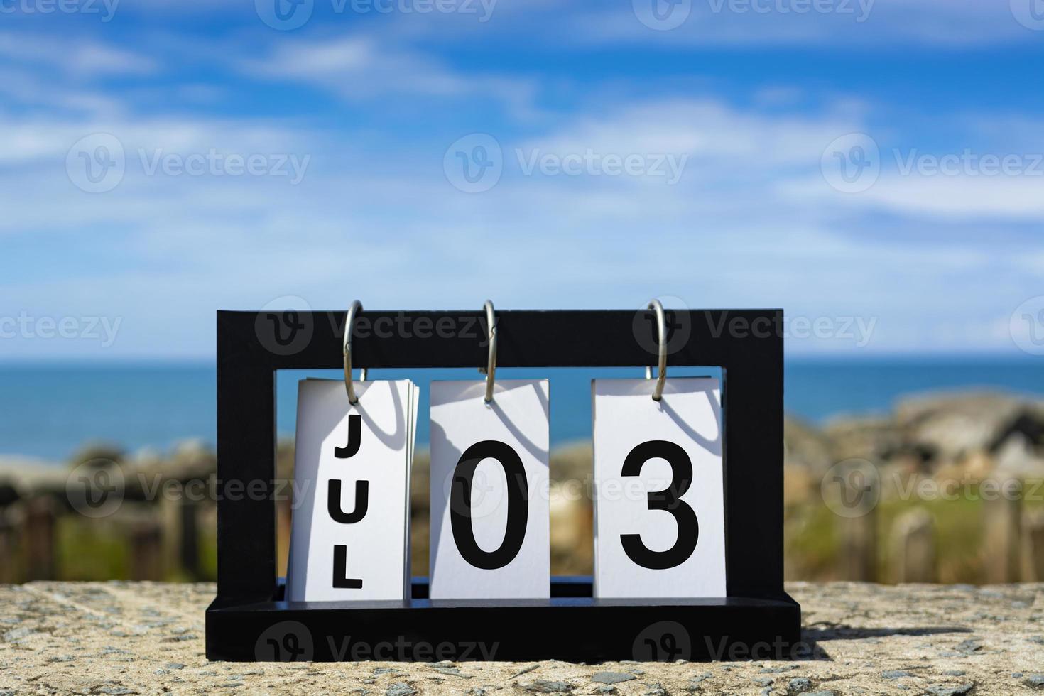 03 de julho texto de data de calendário na moldura de madeira com fundo desfocado do oceano. foto