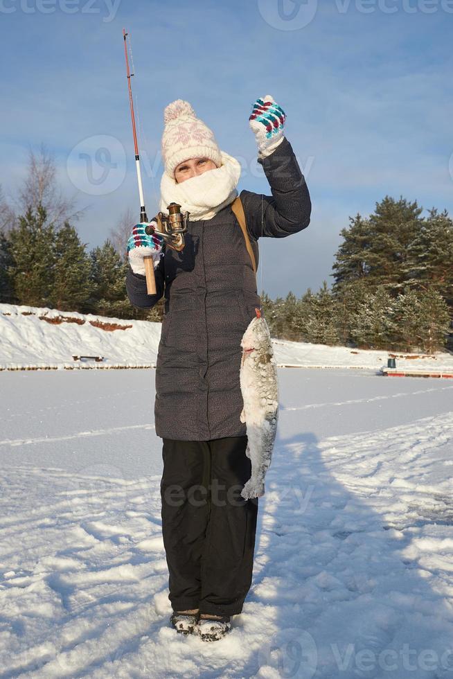 jovem feliz em roupas quentes detém uma truta pega em uma ponta. pesca de inverno. foto