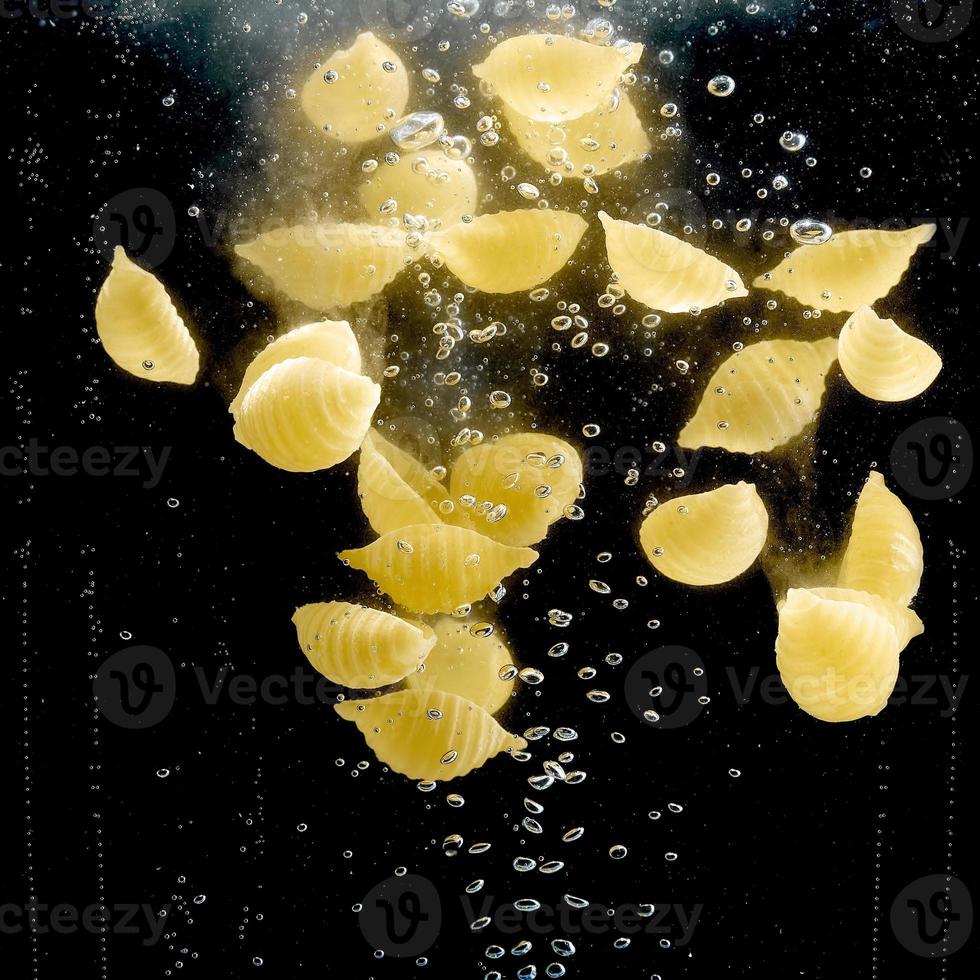 macarrão em forma de concha caindo na água em fundo preto. foto