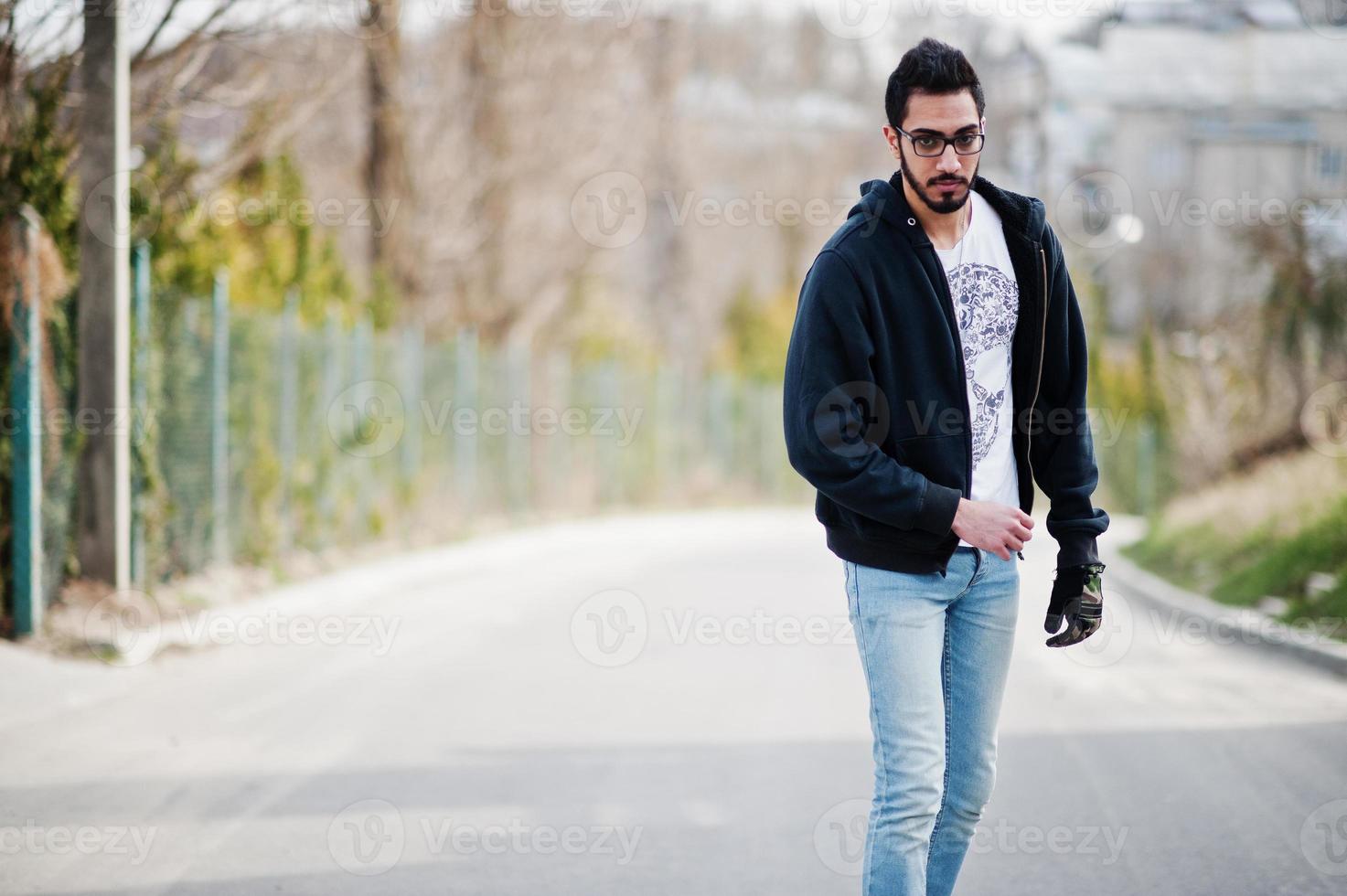 homem árabe de estilo de rua em óculos com longboard longboard na estrada. foto