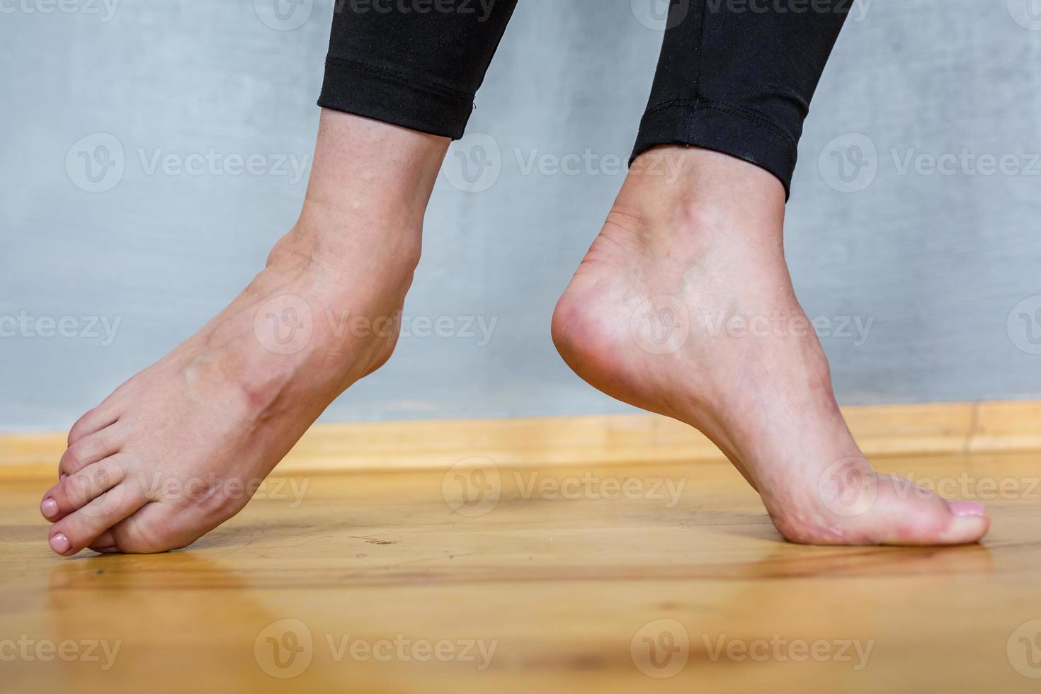 pés femininos descalços em leggings pretas em um piso de madeira foto