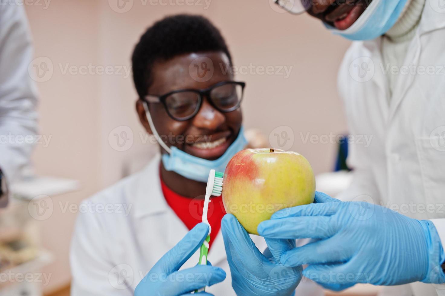 médico masculino americano africano em clínica odontológica com uma maçã e escova de dentes nas mãos. foto