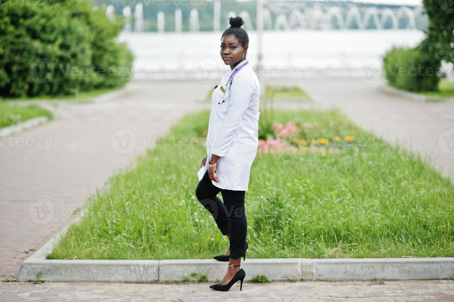 jovem médica afro-americana de jaleco branco com um estetoscópio posou ao ar livre. foto