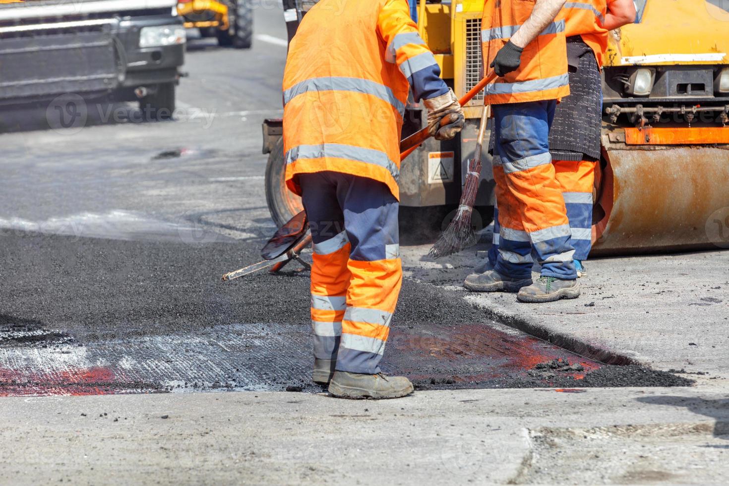 um grupo de trabalhadores rodoviários de macacão laranja está consertando uma seção da pista enrolando asfalto fresco. foto