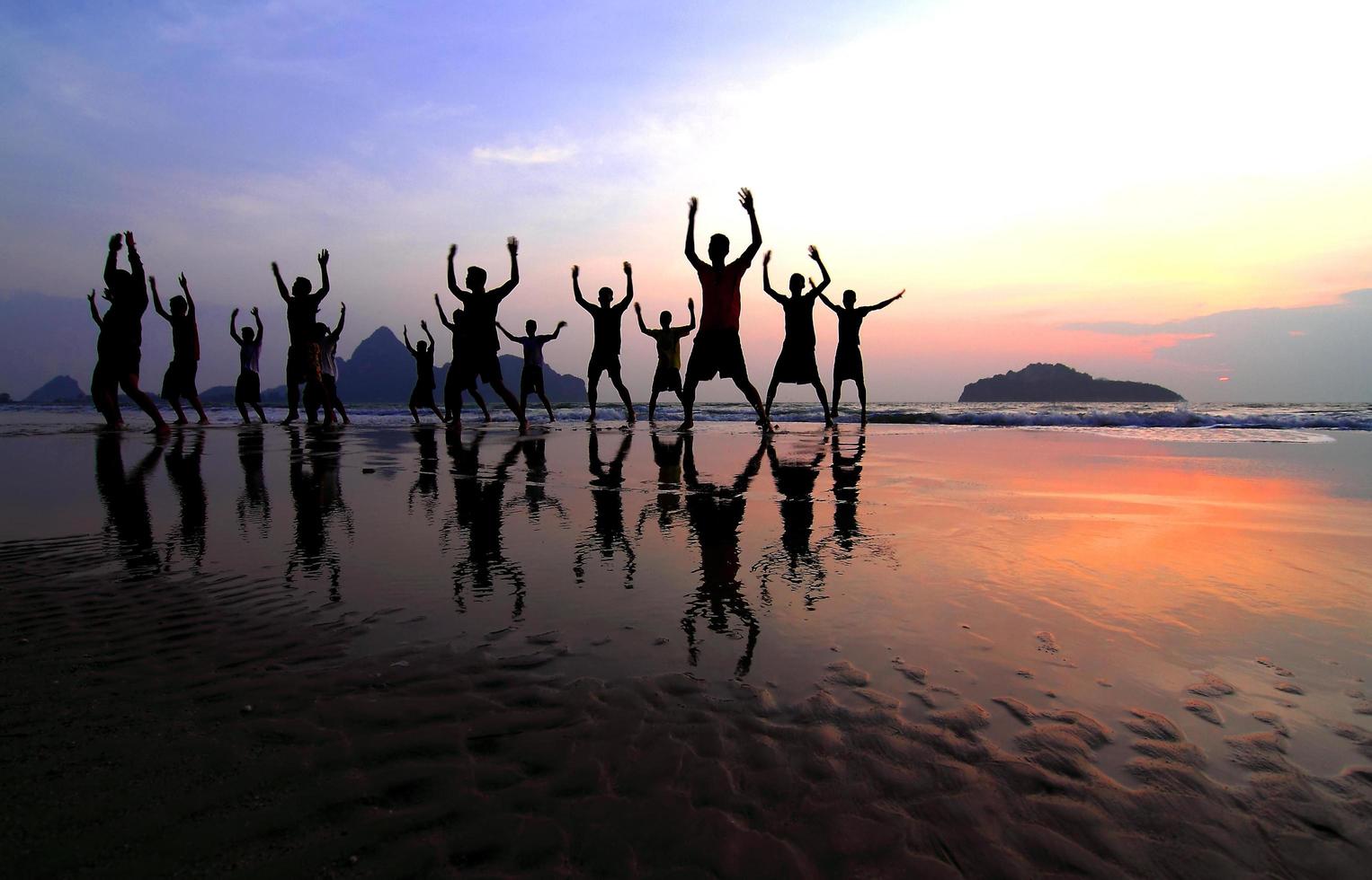 grupo de silhuetas de jovens felizes pulando na praia no belo pôr do sol de verão foto