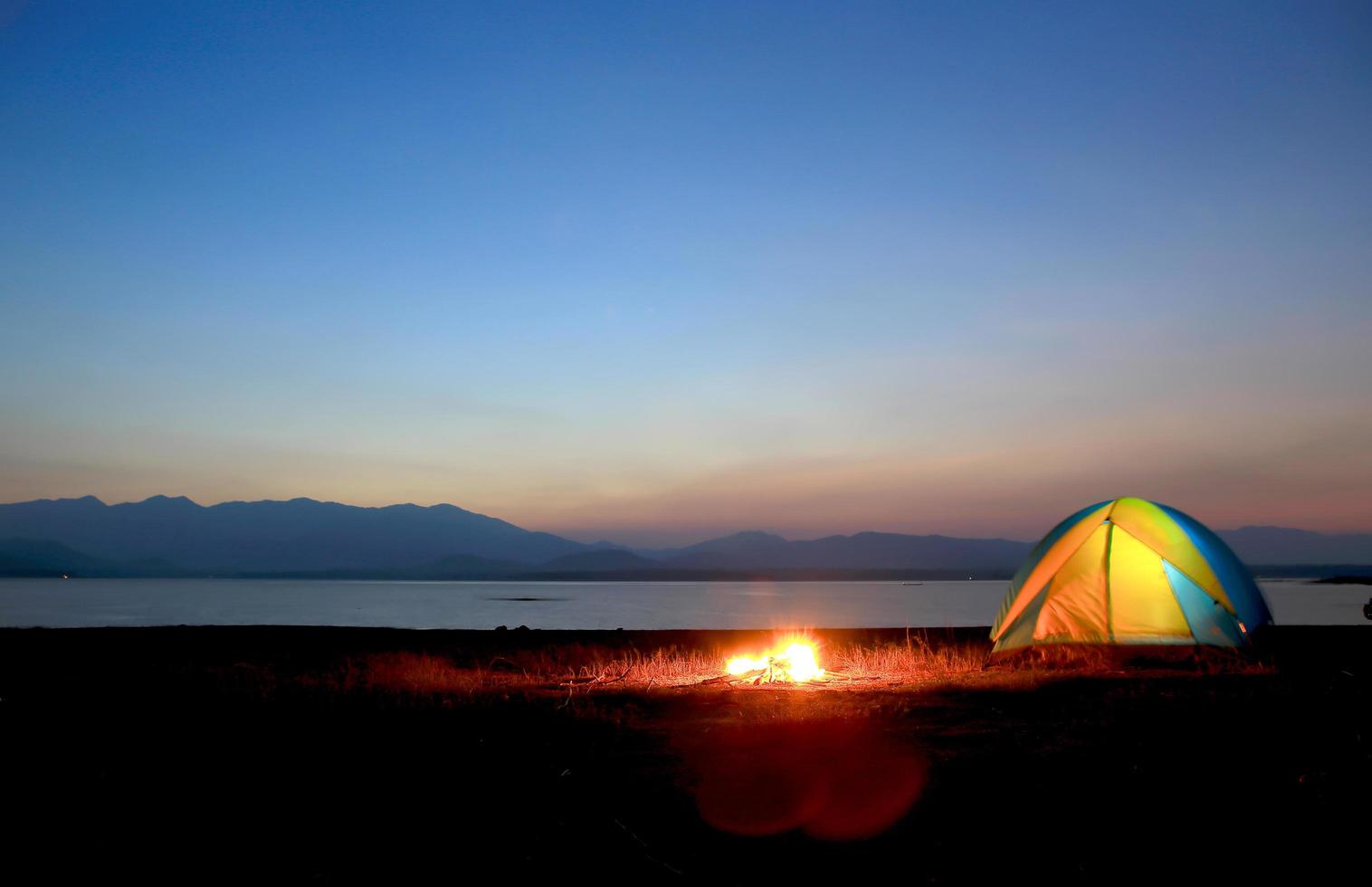 tenda e fogueira ao pôr do sol, ao lado do lago foto