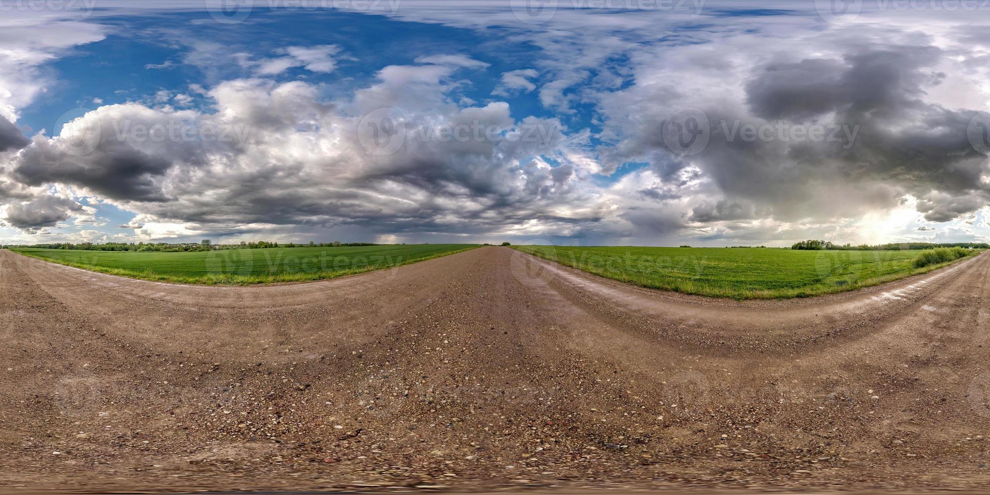 panorama hdri esférico sem costura completo vista de ângulo de 360 graus na estrada de cascalho molhada entre campos em dia de primavera com nuvens de tempestade após chuva em projeção equirretangular, pronto para conteúdo vr ar foto