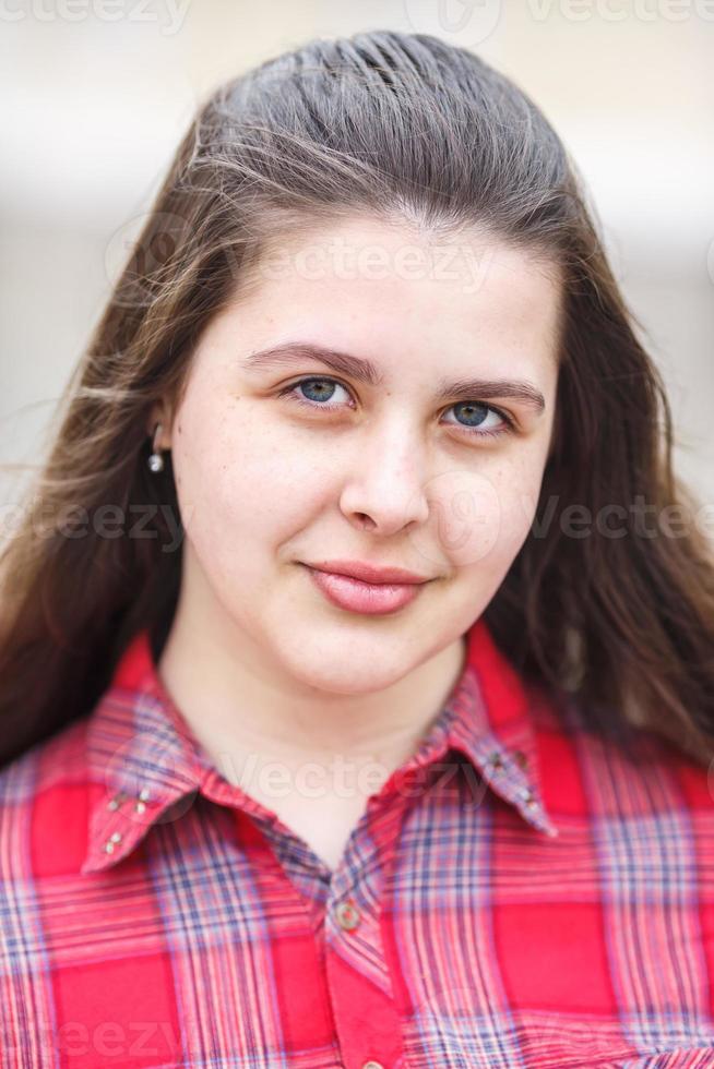 close-up retrato de grande plus size linda menina elegante com jaqueta de couro e camisa xadrez vermelha perto do prédio de tijolos na rua urbana como pano de fundo foto