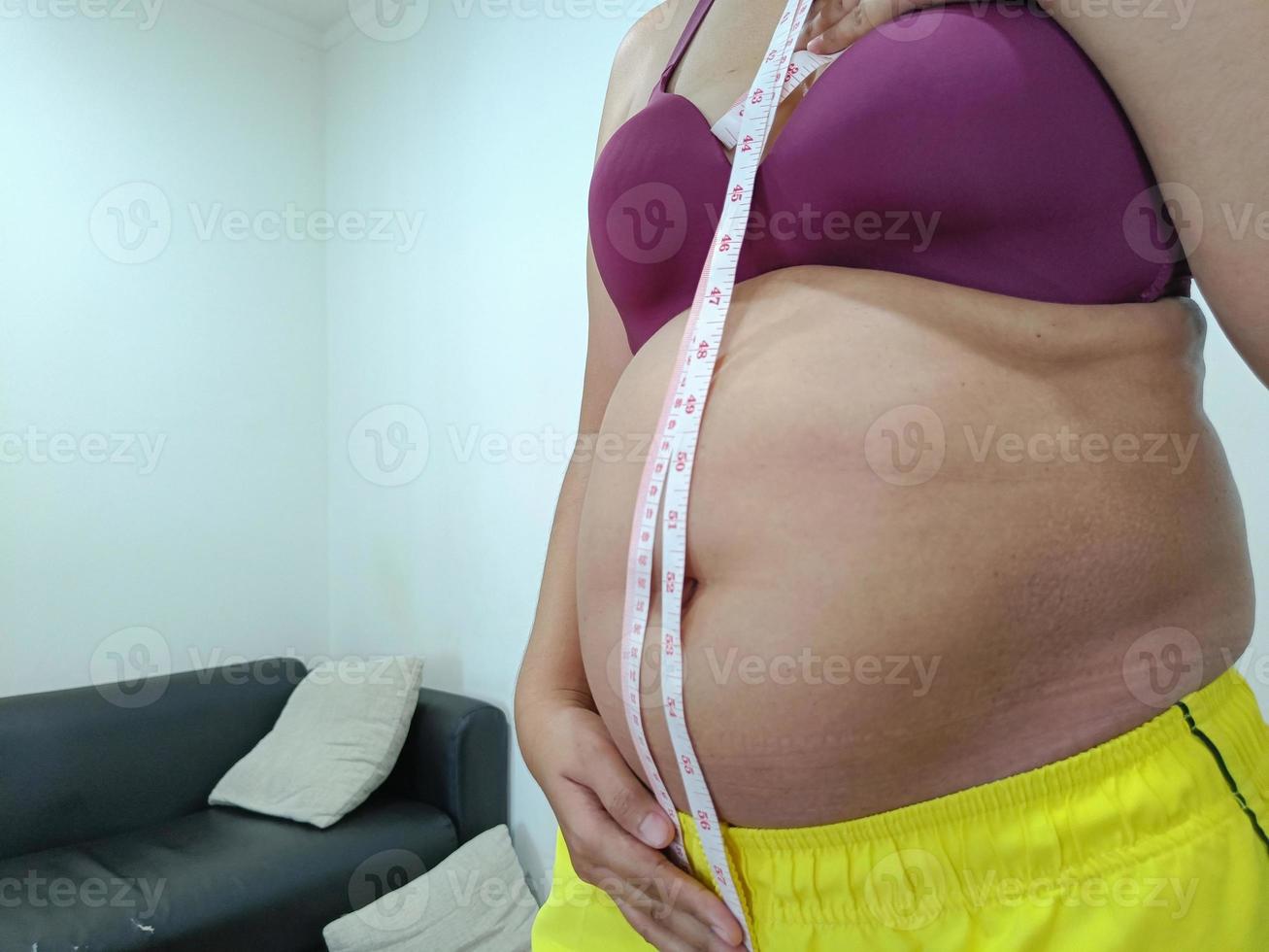 vista frontal. mulher asiática gorda em pé mostrando sua barriga foto